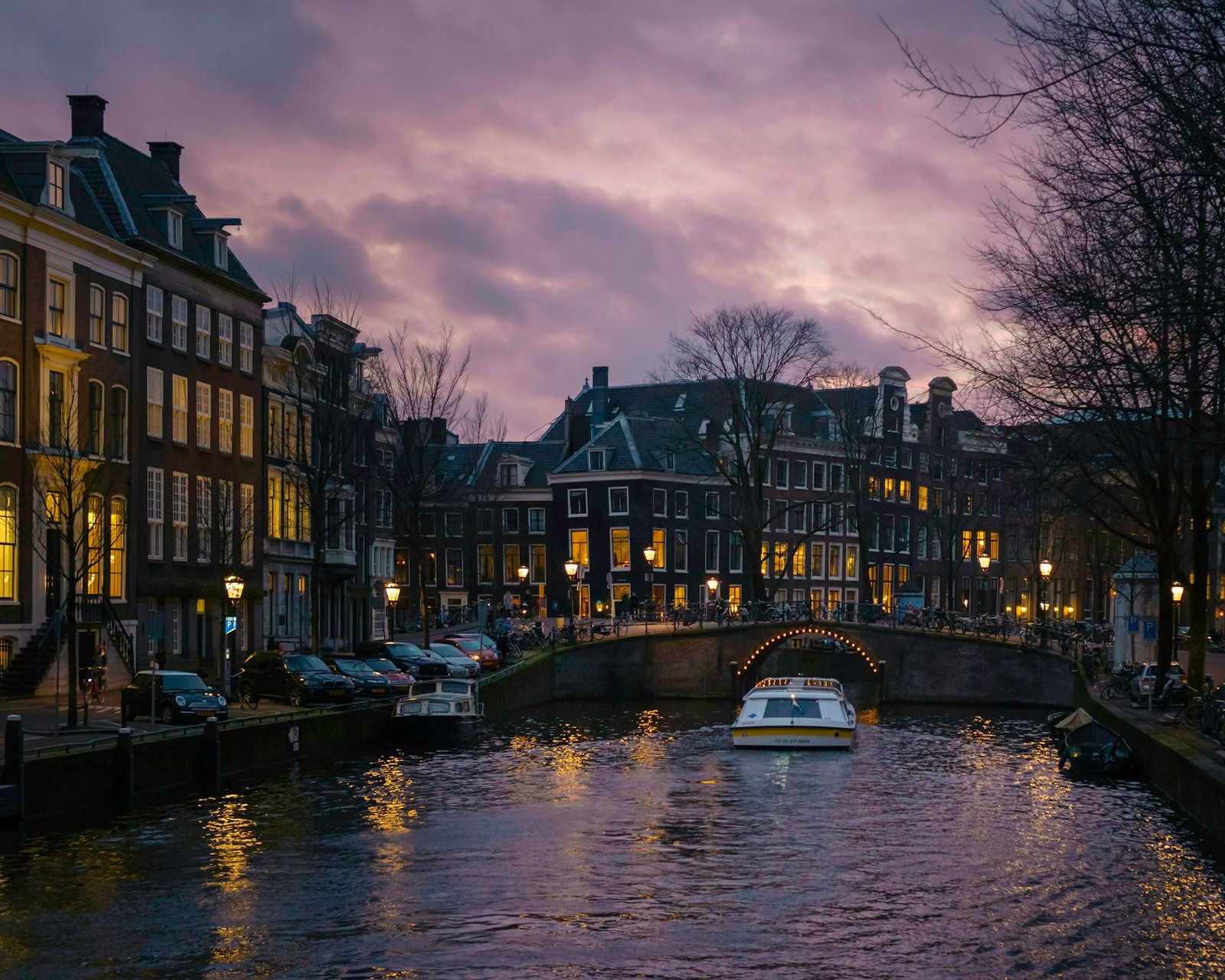 Quiet Amsterdam canal at dusk, warm lights, soft pink sky