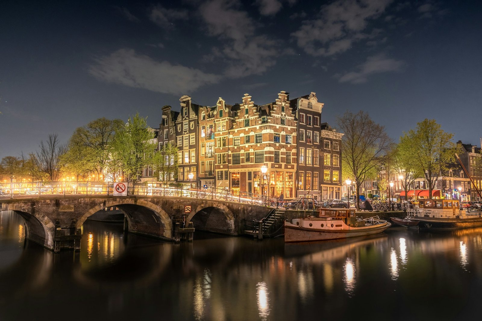Amsterdam canal house facade lit warm yellow at dusk, reflected in water