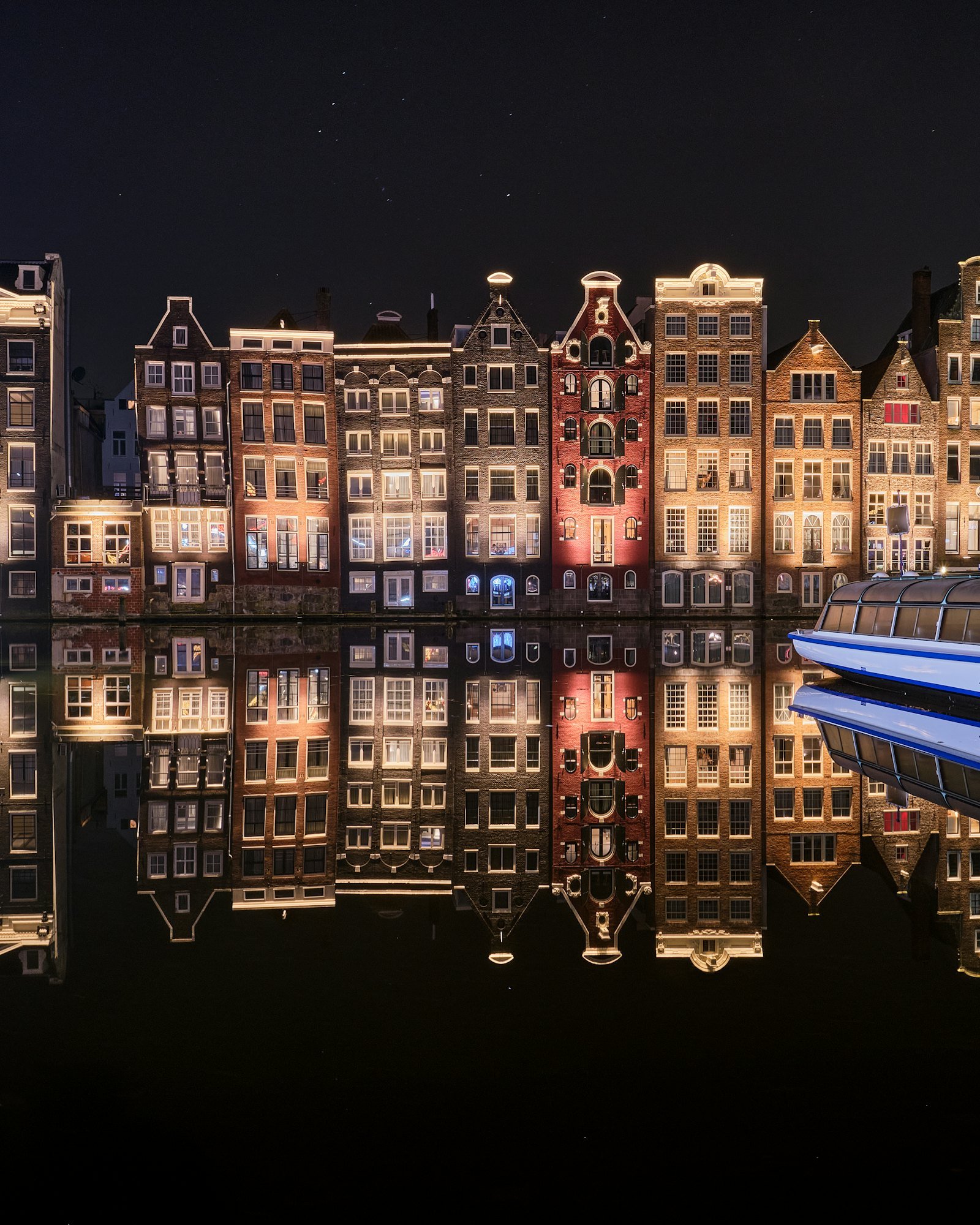 Amsterdam canal houses lit warm at night, mirror reflection in still water