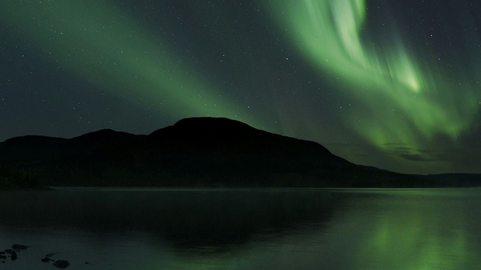 Aurora borealis over a lake in Swedish Lapland, fell ridge silhouetted against the green arc