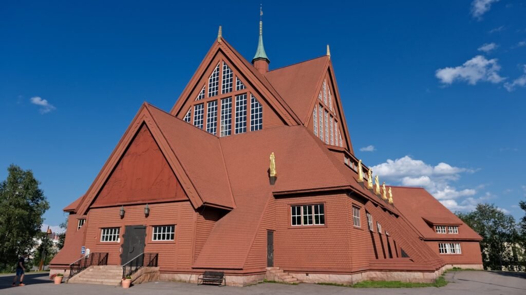 Kiruna Church seen in full, dark red wooden shingles and tent-shaped roof, gilded statues along the eaves