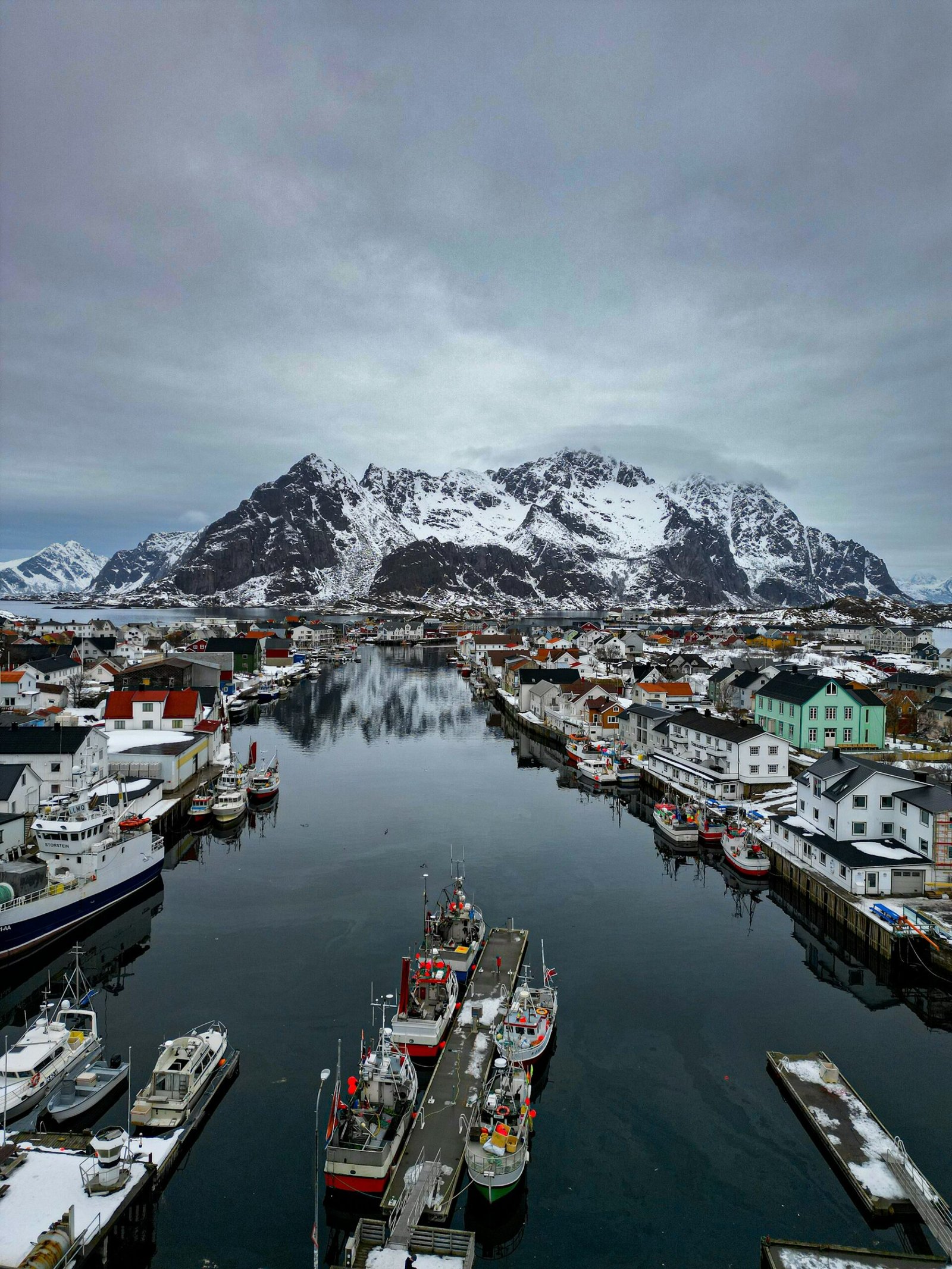 Working harbour full of fishing boats under a snow-covered mountain, Lofoten, winter light