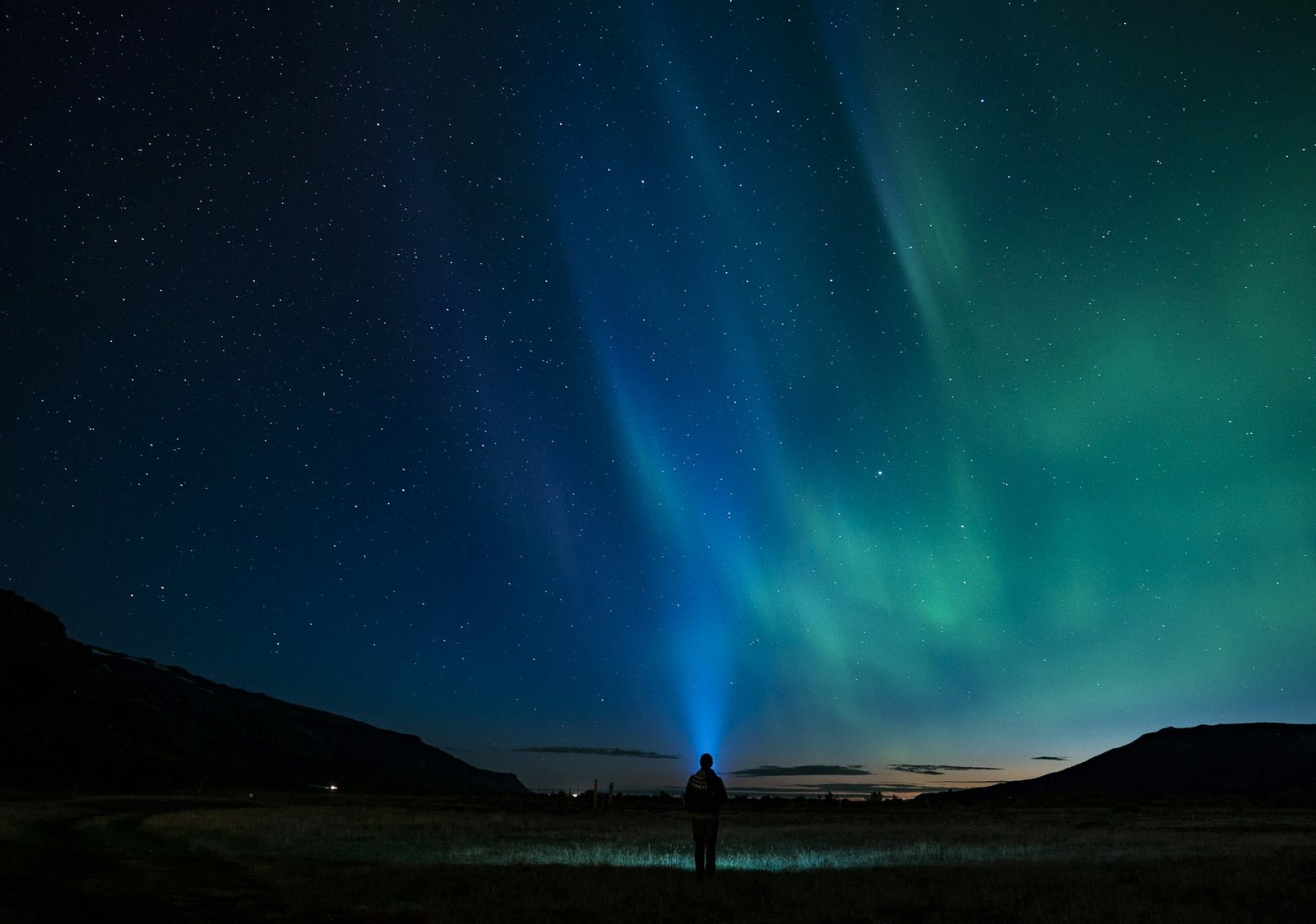 Silhouette of a person standing under the aurora, conveying scale and cold