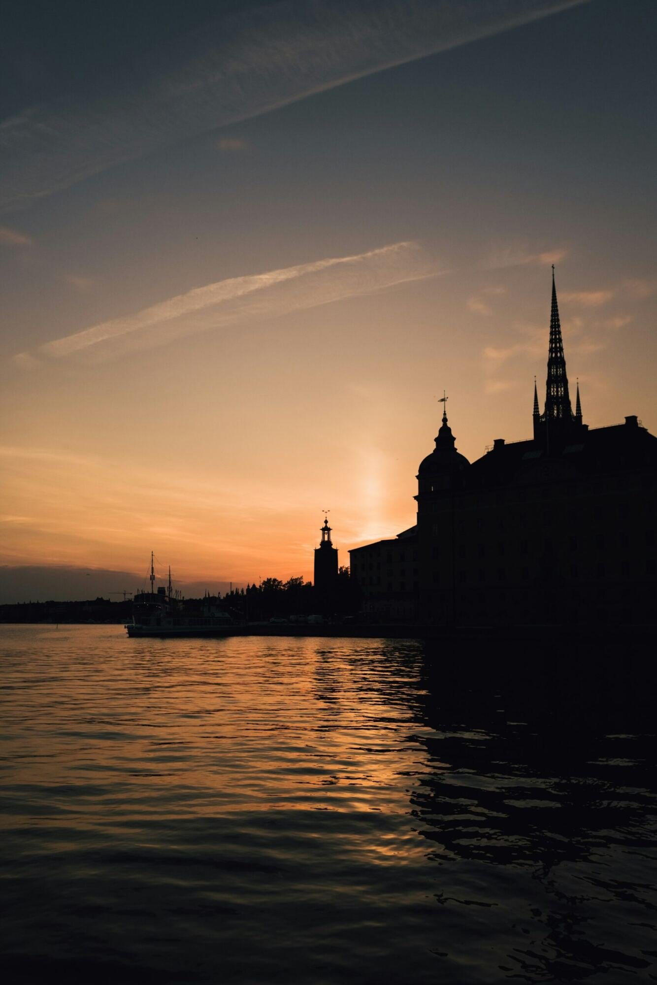 Silhouette of Gamla Stan spires against an orange sunset sky, reflected in the still water