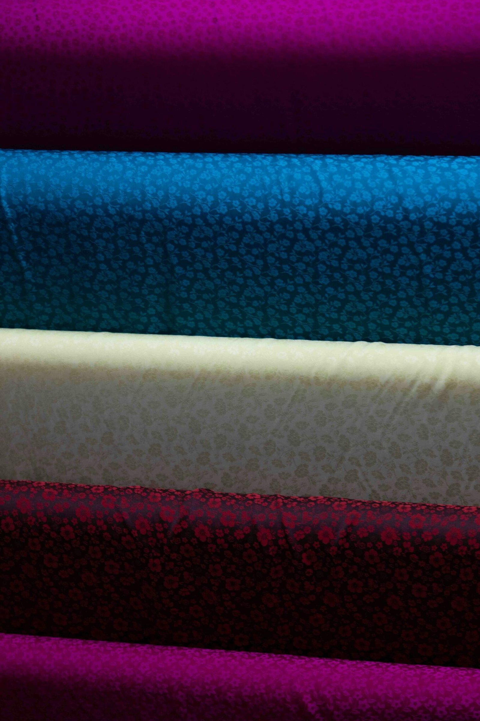 Colourful woven fabric rolls stacked on a shelf, reminiscent of a textile archive