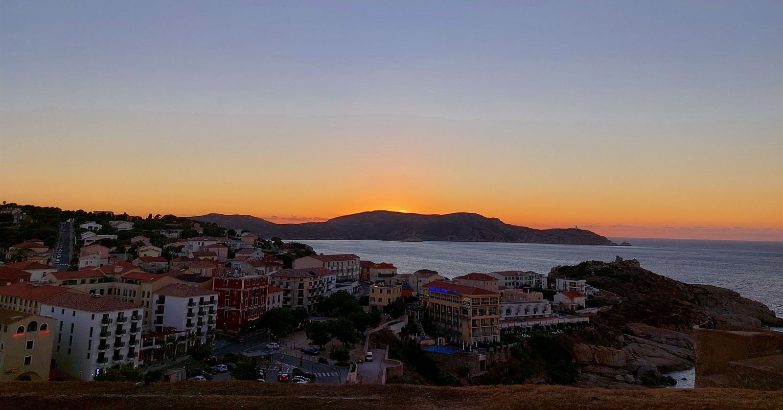 Sunset over Calvi, the town in shadow below and the sun dropping behind the headland