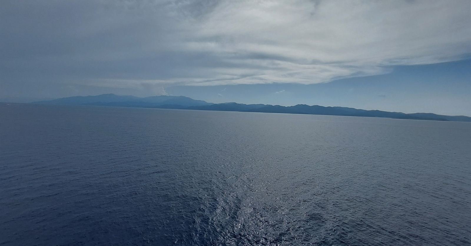 The Corsican coast of Cap Corse seen from the ferry, low mountains under an overcast sky