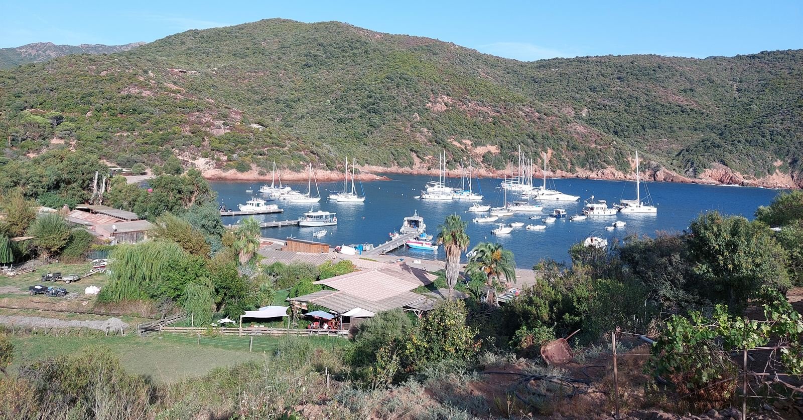 The sheltered bay of Girolata, sailing boats at anchor below red porphyry cliffs and a small hamlet
