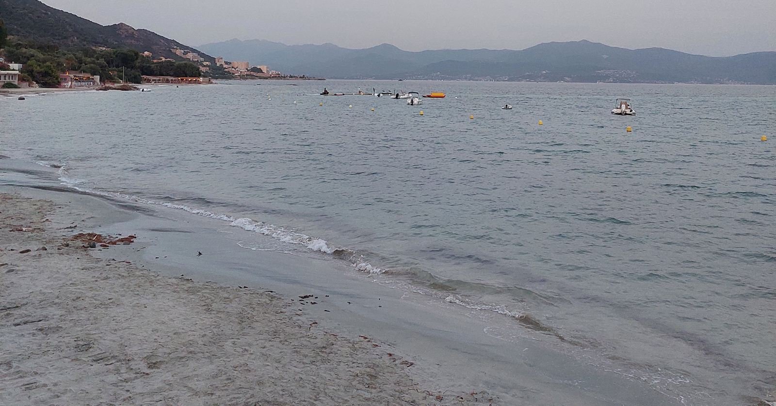 A quiet beach at dusk on the Gulf of Ajaccio, small boats moored offshore and mountains across the bay