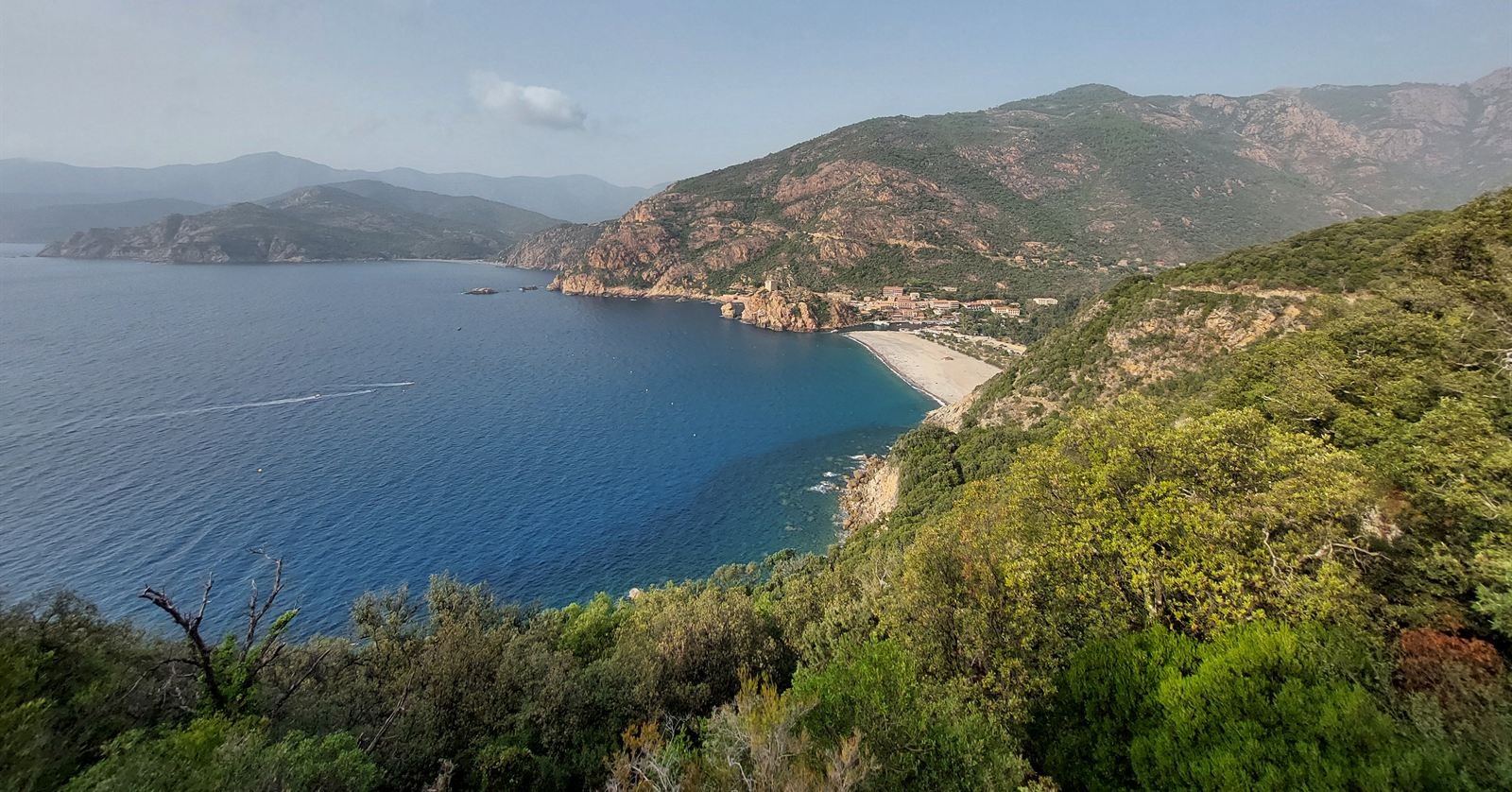 The Gulf of Porto from the corniche road, a pebble beach below the village and red mountains behind