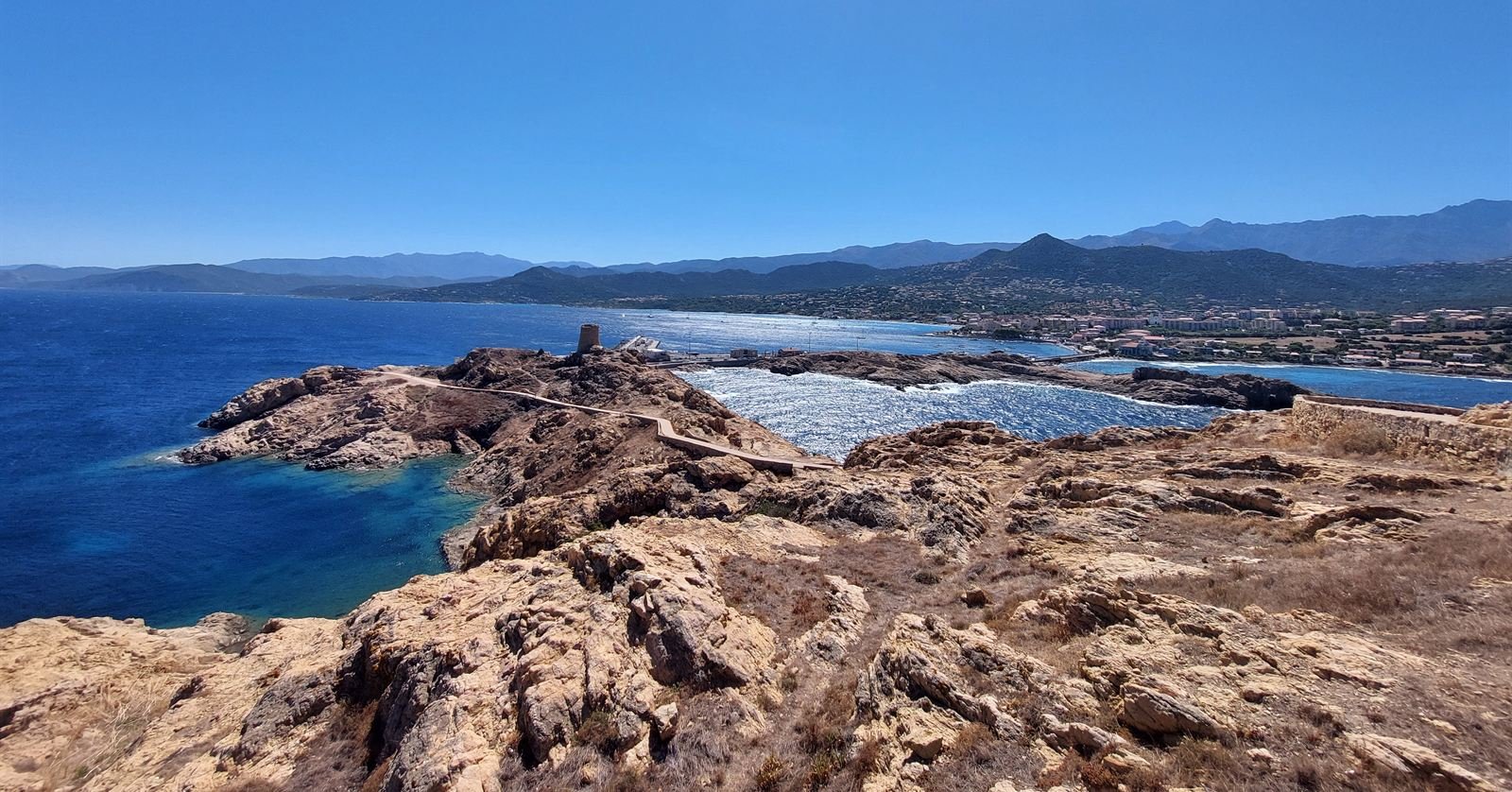 The Genoese tower on the rocky headland at L'Île-Rousse, with the Balagne coast and mountains beyond