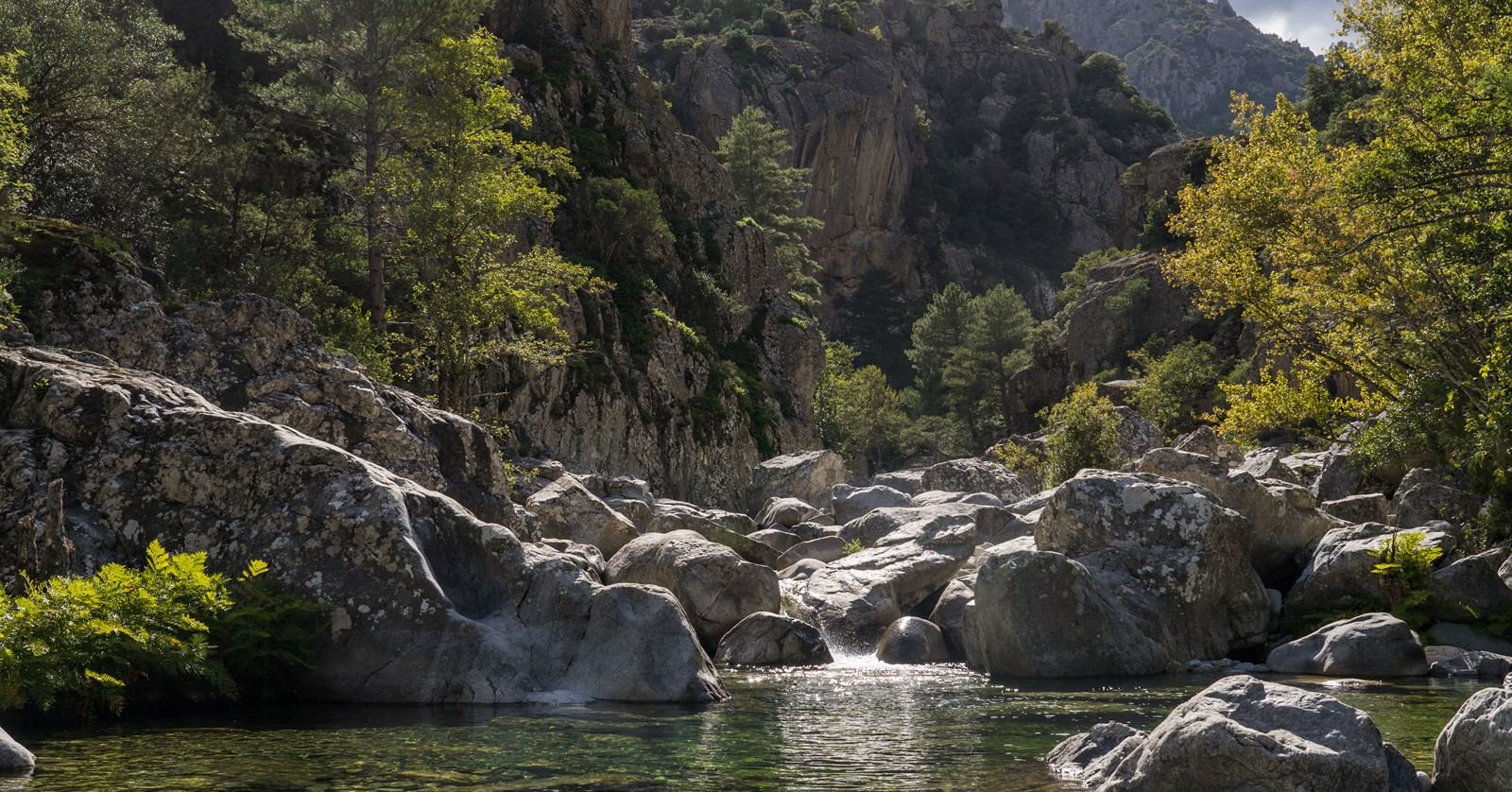A clear pool beneath a small waterfall between granite blocks in a gorge west of Corte
