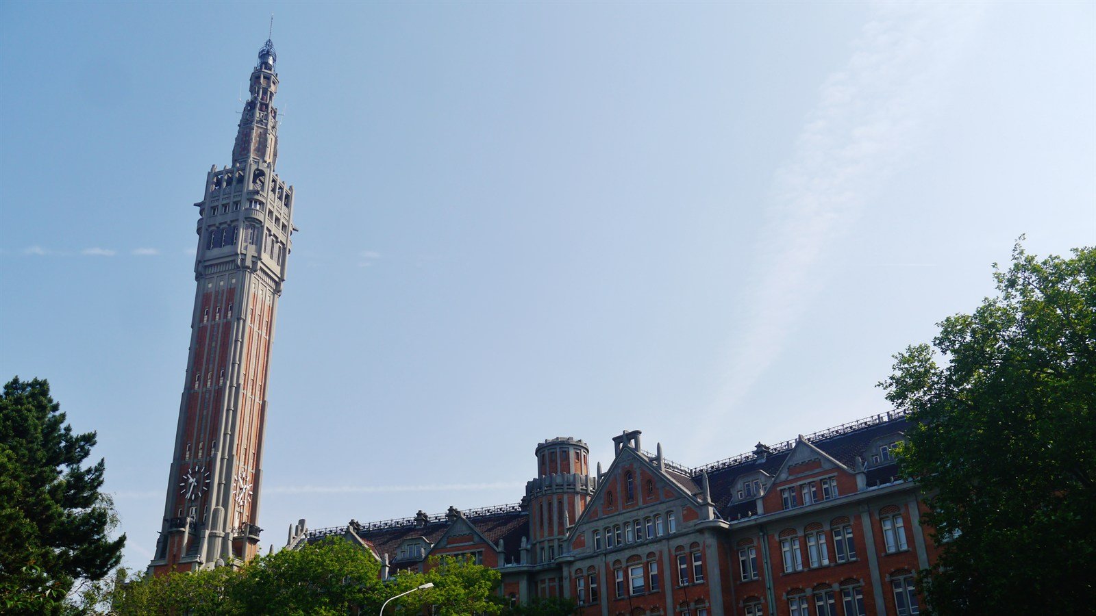The belfry of Lille town hall seen from the square below, the stepped Flemish gable and brick facade of the building to its right under a clear sky